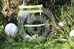 Close up of lonely isolated green wooden folding chair in the garden with grasses, green reed, electric round lamps