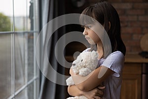 Close up lonely little girl hugging toy, looking out window