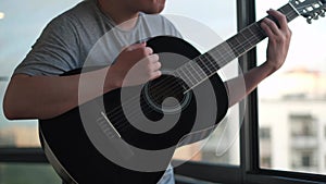 Close up of lonely man playing guitar against an opened window. Concept. Young musician playing chords and songs on the