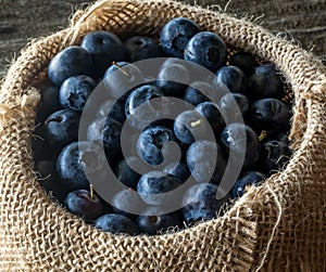 A close up look into a burlap bag filled with fresh blueberries.