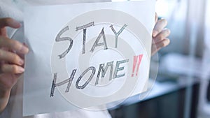 Close-up looks out the window, holding a sheet of paper with the inscription #stayhome