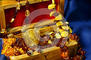 Close-up a lot of jewelry from amber in wooden chest on a blue background.