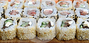 Close-up of a lot of sushi rolls with different fillings lie on a wooden surface. Macro shot of cooked classic Japanese food with