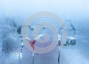 Close-up on love heart and home condensation lettering against sweaty window glass. Hand draws a heart and a house on a foggy