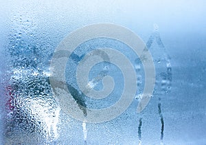 Close-up on love heart and home condensation lettering against sweaty window glass. Hand draws a heart and a house on a foggy