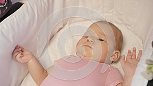 CLOSE UP: Lovely baby girl with big blue eyes lying in a comfortable carriage.