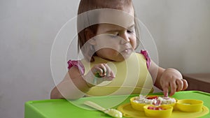 Close up of lovely baby girl eating have breakfast eggs vegetables sausage by herself at home. Adorable possitive happy