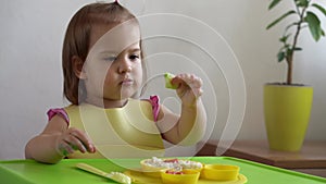 Close up of lovely baby girl eating have breakfast eggs vegetables sausage by herself at home. Adorable possitive happy