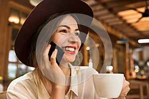 Close up of a lovely girl in hat sitting at the cafe table indoors, holding cup of tea,