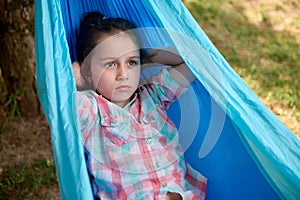 Close-up lovely little child girl relaxing on blue hammock in the backyard, enjoying a weekend outdoors. Kids. Leisures