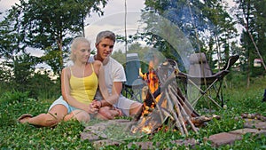 CLOSE UP: Lovely shot of a young tourist couple snuggling by the warm campfire.