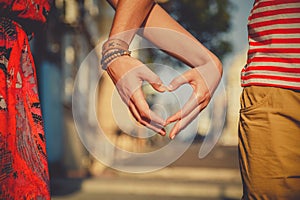 Close up of loving couple making heart shape with hands at city street. Summertime