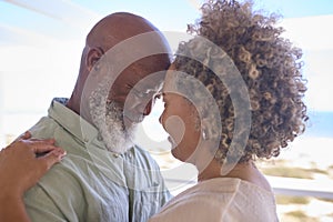 Close Up Of Loving Mature Couple Hugging In Beachfront House Overlooking Ocean For Summer Vacation photo