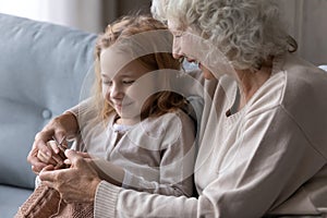 Close up loving mature grandmother teaching little granddaughter to knitting