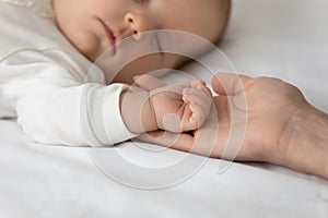 Close up loving mother holding sleeping small baby hand