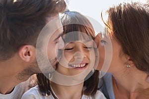 Close up of loving parents kiss small daughter on cheeks