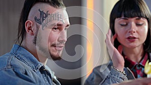 Close-up of loving tattooed millennial man sitting with girlfriend in bar talking and smiling. Positive Caucasian