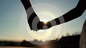 Close-up of loving young couple hand-holding and walking towards sunset on background of cloudless sky and bright