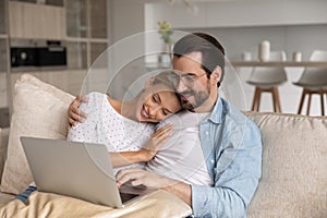 Close up loving young couple hugging, using laptop together