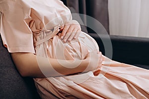 Close up of loving young pregnant woman sitting on couch stroking big belly, expressing love and care to unborn baby, expecting