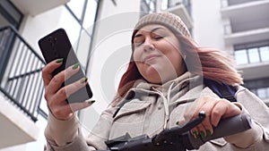 Close-up low-angle view of delivery woman with thermo backpack using navigation app on mobile phone, riding order on