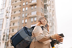 Close-up low-angle view of food delivery woman with thermo backpack holding mobile phone waiting next order standing