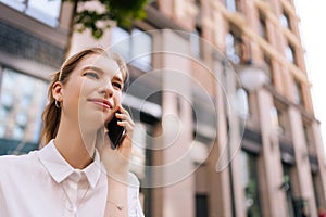 Close-up low-angle view of loving pretty young woman talking on mobile phone with boyfriend on city street on background