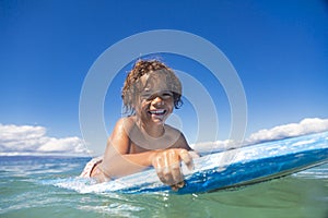 Close up low-angle view of a Smiling diverse young boy boarding in the beautiful blue ocean