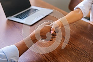 Close-up low-angle view of unrecognizable businesswoman and businessman closing deal and shaking hands in agreement.