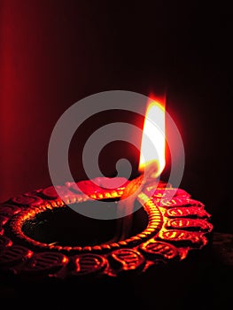 Close up low key diwali oil clay lamp on a dark orange black background with bright orange red light