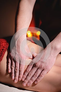 Close-up low key on woman`s thigh massage in a professional premium spa salon, man masseur does in a dark room on the