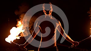 Close-up. Low key. Young male with long hair and bare torso rotates burning torch outdoors on a black night video slow