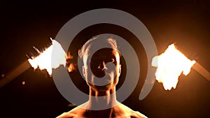 Close-up. Low key. Young male with long hair and bare torso rotates burning torch outdoors on a black night video slow