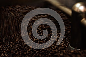 Close-up and low speed shutter blurred to capture the movement of dark roast coffee bean moving in rotating mixing coffee roaster