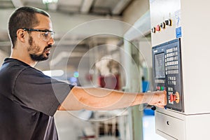 Close-up of machinist pressing emergency stop button on control panel