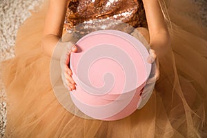 Close up, macro. Hands of a little girl in a gold dress hold / hold out a pink round gift box. Christmas concept