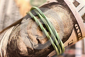 close up macro of paper currency roll of hundred dollars knitted by rubber band