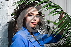 Close up, macro. Portrait of a girl in a business blue suit, the shadow of the leaves of a green tropical plant falls on her face