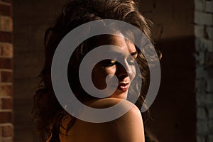 Close up, macro. Portrait of sensual pin-up model with a naked rounded shoulder. Brown brick wall in the background