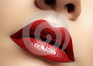 Close-up macro shot of female mouth. Glamour red lips Makeup with sensuality gesture. Metalic gloss lipstick