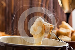 Close up, macro. Traditional french cheese fondue. Crouton dipped into stemy-hot cheese fondue on a long-stemmed fork. Copy space