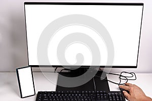 Close up macro view of hand man using computer monitor with mockup image blank screen and cell phone.