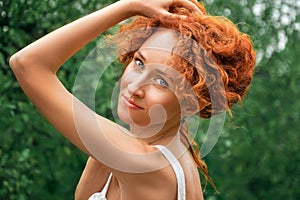 Close up, macro. A beautiful girl in a white lace dress gracefully holds in her hands a cascade of red curls. Face with natural