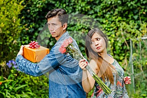 Close up of mad woman holding flowers and mad man holding a gift back to back ignoring each other, friend zone concept