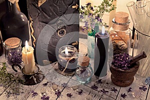 Close up of magic book, dry flowers, glass jars and burning candles on the table