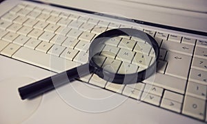 Close up of a magnifying glass on an old laptop keyboard. Computer search engine. Browsing network for answer to every question.