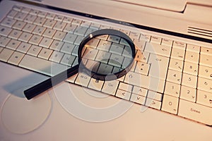 Close up of a magnifying glass on an old laptop keyboard. Computer search engine. Browsing network for answer to every question.