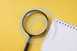 Close up  magnifying glass and white spiral notepad on a table yellow background