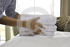 Close-up of maid hands putting fresh white bath towels on the bed sheet. Housekeeper service cleaning in the hotel room.