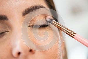 Close-up of a make-up artist applying eye shadow to her client.